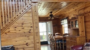 A wooden cabin interior with a staircase, a dining area, a living room with a red sofa, and a patterned rug. - Boo Boo's Cabin - Charming Lake Front Cabin located 5 miles to Helen, GA!  (Cleveland)