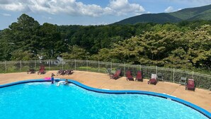 A swimming pool with lounge chairs and a view of a forested hillside. - Boo Boo's Cabin - Charming Lake Front Cabin located 5 miles to Helen, GA!  (Cleveland)