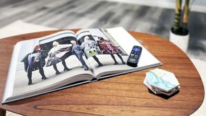 A magazine on a wooden table with a cityscape photo, a remote control, and a small plant.