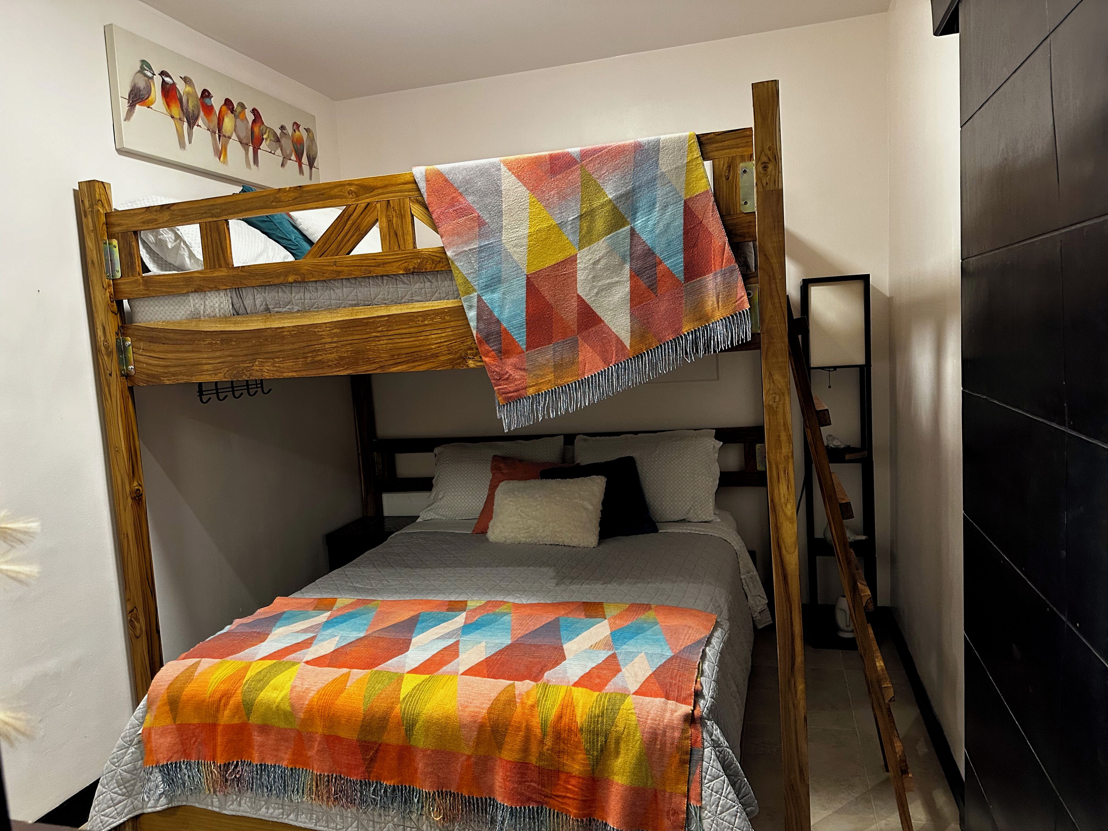 A bunk bed with a colorful quilt, a wooden headboard, and a wall-mounted shelf with a lamp.