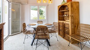 A dining area with a round table, wicker chairs, and a wooden cabinet with shelves.