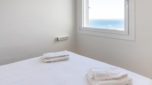 A minimalist room with a bed, a window with a view of the sea, and a power outlet on the wall.