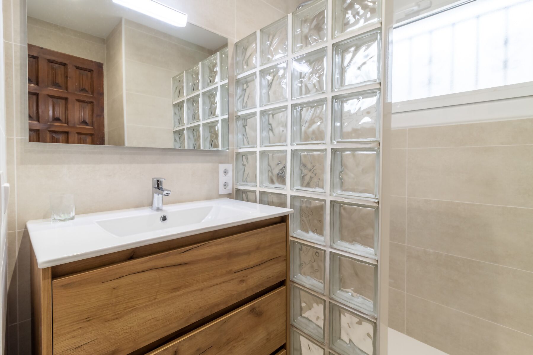 Un baño con tocador de madera, un lavabo blanco y un espejo grande.