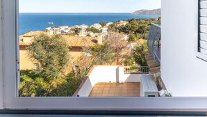 A view from a window overlooking a coastal town with buildings, trees, and a clear blue sea.