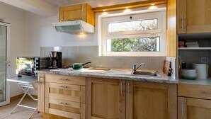 A modern kitchen with wooden cabinets, a built-in oven, a coffee maker, and a window providing natural light.