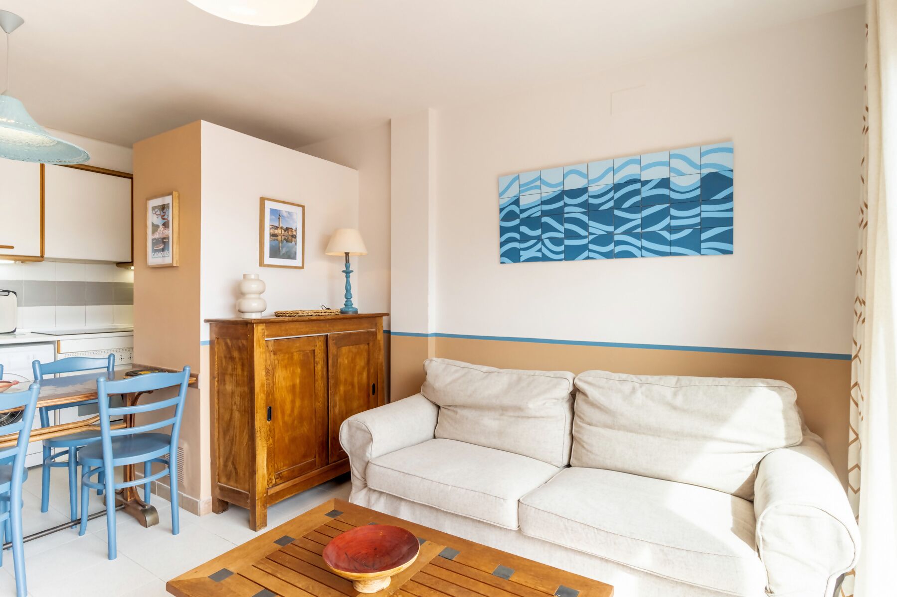 A living room with a white sofa, a wooden coffee table, and a blue dining area with chairs.