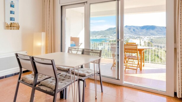 A dining area with a table and chairs, a balcony with a view of mountains, and a sliding glass door. - Cap Ras 04.3 - Apartment with terrace and sea view (Llança)