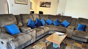 Un sofá modular con cojines azules y una mesa de centro de vidrio en una sala de estar con piso de baldosas.