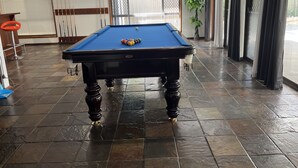 Una mesa de billar con superficie de fieltro azul, rodeada por un piso de baldosas de piedra.
