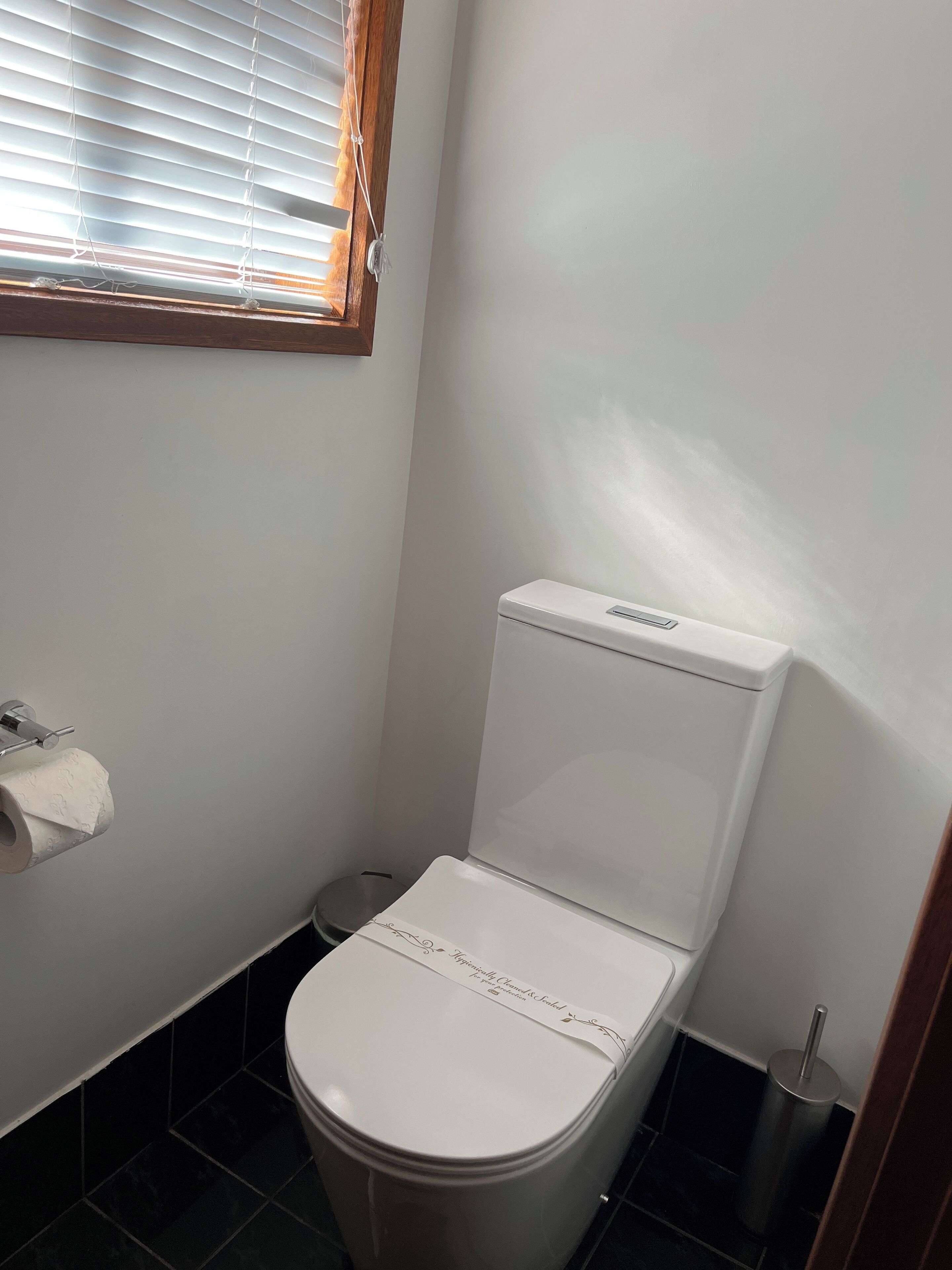 Une petite salle de bain propre, avec des toilettes blanches, un porte-rouleau de papier toilette et une poubelle.