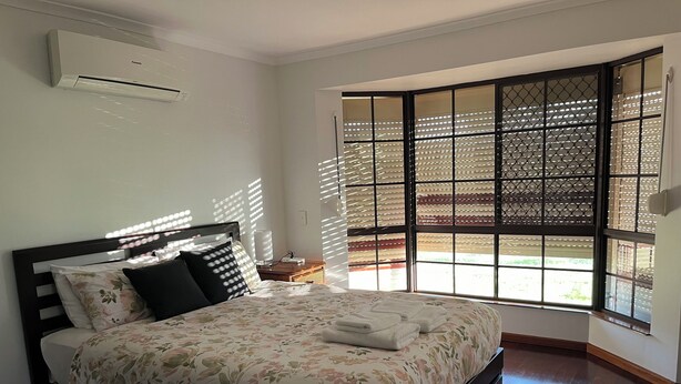Un dormitorio con cama, mesita de noche, ventana con persianas y unidad de aire acondicionado.