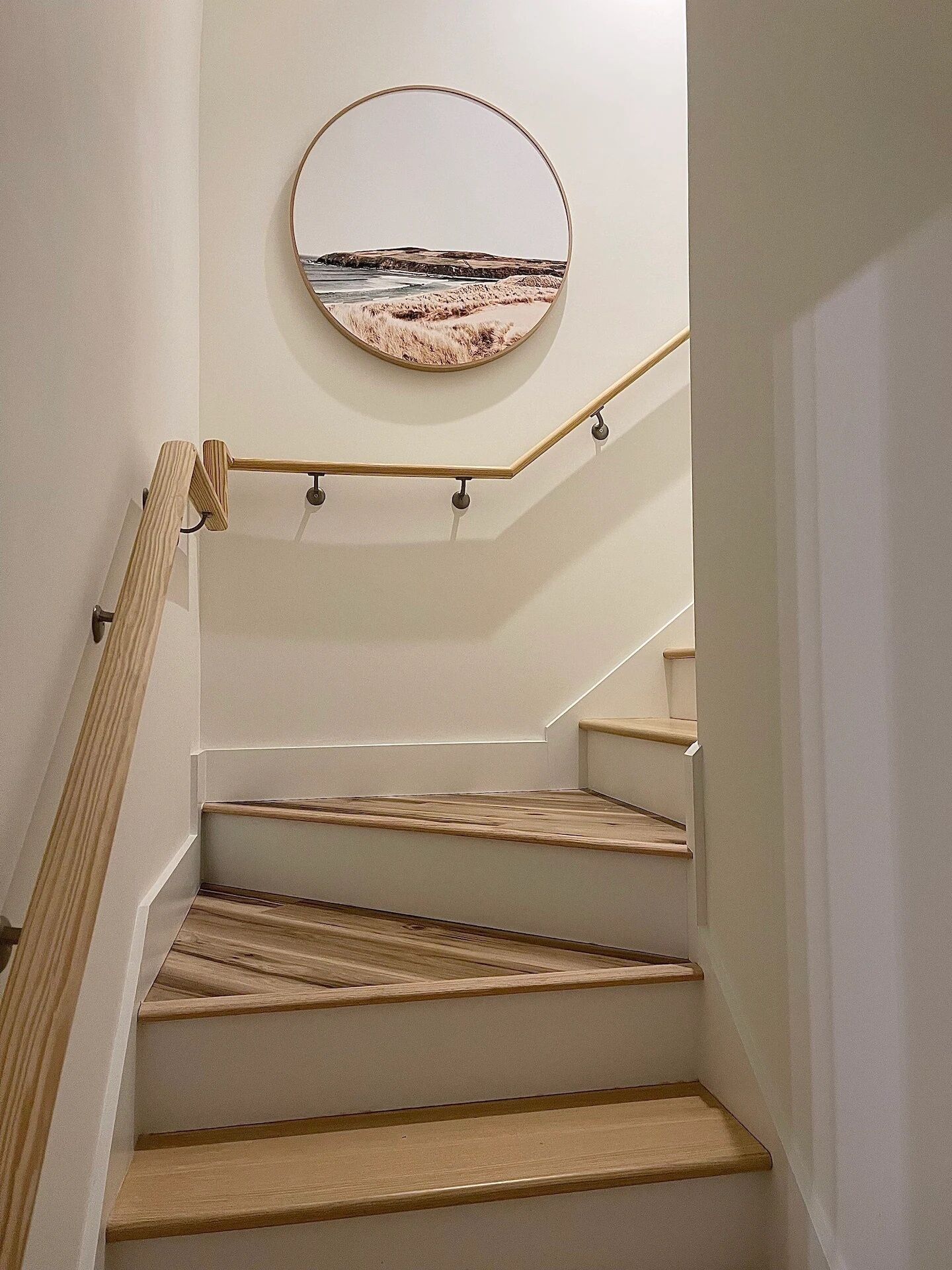 Eine Treppe mit Holzstufen und Handlauf, die zu einer Zwischenebene mit einem rundem, an der Wand befestigten Spiegel führt.