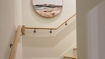 Eine Treppe mit Holzstufen und Handlauf, die zu einer Zwischenebene mit einem rundem, an der Wand befestigten Spiegel führt.