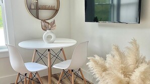 Een eetgedeelte met een ronde tafel, twee stoelen, een decoratieve spiegel en een televisie aan de muur.
