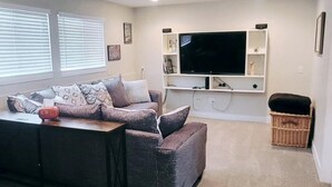 A living room with a grey sofa, a TV mounted on a white shelf, and a wicker basket. - Pikes Peak Panorama View (Colorado Springs)