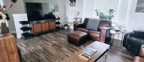Ein Wohnzimmer mit Couch aus Leder, Fernseher und einem Holztisch.
