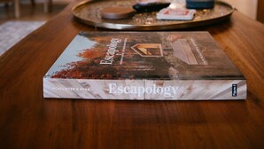 A book titled 'Escapology' on a wooden table in a well-lit room with modern furniture and a chandelier. - Hickory Hill Round House: Indoor POOL, mins from South Holston River, with view  (Bluff City)