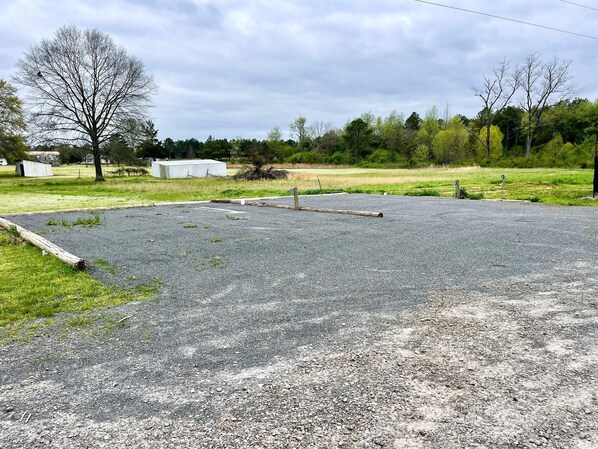 An empty parking lot with gravel surface, surrounded by grassy areas and trees.