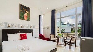 A hotel room with a large bed, a small table with chairs, a refrigerator, and a balcony with a view of the city. - Hoa Hong Hotel (Ho Chi Minh City)