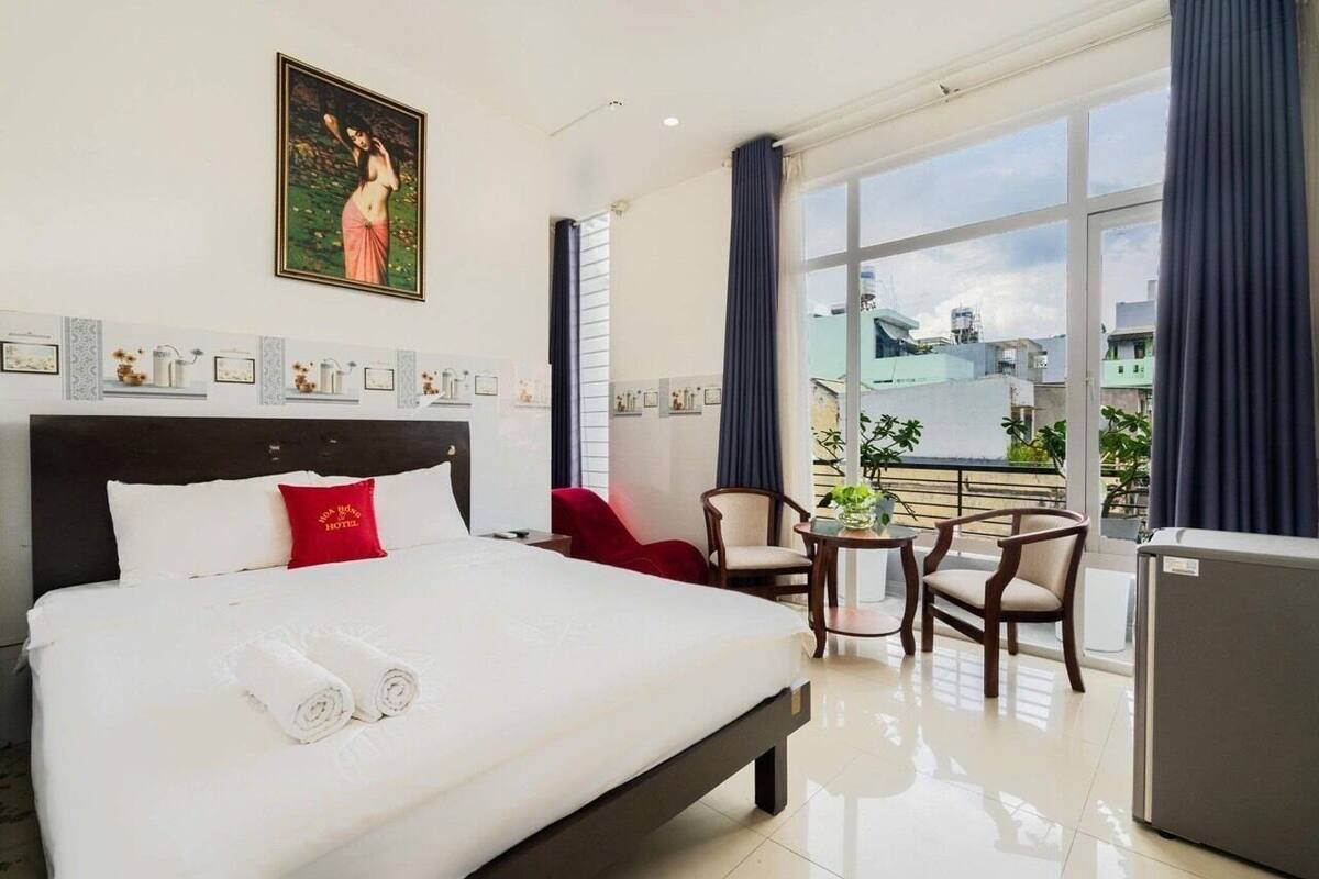 Een hotelkamer met een groot bed, een kleine tafel met stoelen, een koelkast en een balkon met uitzicht op de stad.