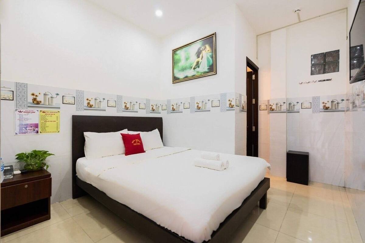 Hotelkamer met een groot bed, nachtkastje, klein tafeltje en een wandplank met ingelijste foto's en notities.