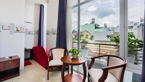 A modern living room with a large window, two wooden chairs, a small table with a plant, and a red chair. - Hoa Hong Hotel (Ho Chi Minh City)