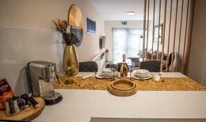 Enjoy a meal in the hotel room's dining area, which features a coffee maker, vase with dried plants, and a table set with plates, glasses, and champagne.