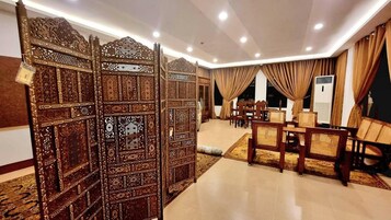 A hotel lobby with a traditional wooden partition, a seating area with wicker chairs, and a carpeted floor.