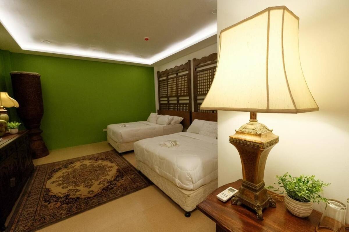 Une chambre d’hôtel avec deux lits simples, un mur vert, une lampe de style traditionnel et un tapis décoratif.