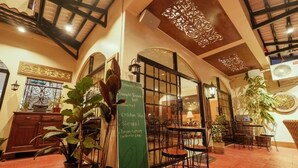 Een restaurant met een hoge plafond, gebogen ramen en een menubord waarop gerechten staan vermeld zoals 'Simpel Ontbijt' en 'Kippenhuid'.