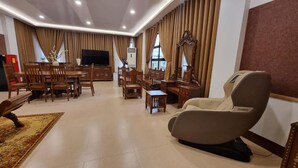 Een ruime woonkamer met een grote houten eettafel, comfortabele zithoek, een massagestoel en een televisie.