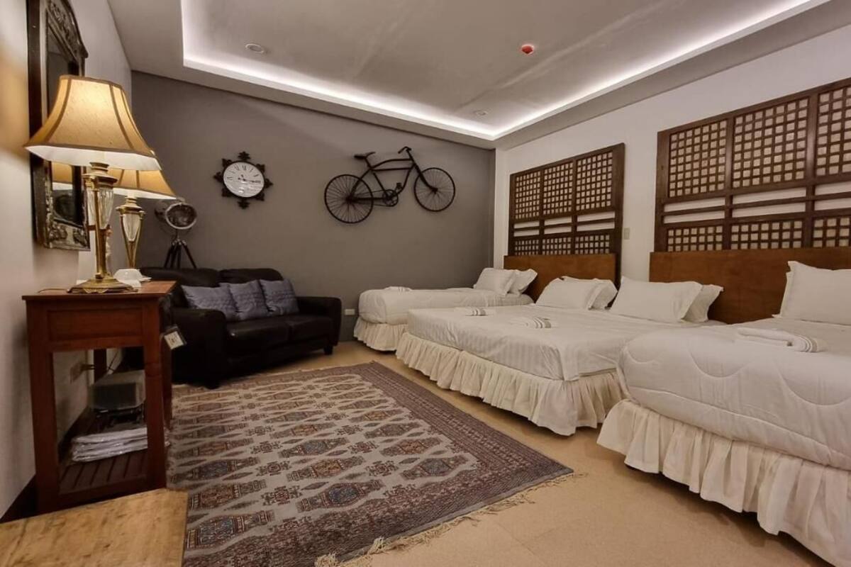 Une chambre d’hôtel avec deux lits, un bureau, une lampe, un vélo et un panneau décoratif mural.