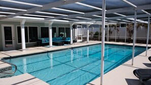 Una piscina con un porche techado, un espacio de descanso con un sofá azul y vistas del paisaje circundante.