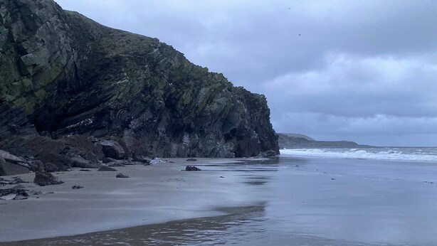 A beach with a rocky cliff and waves.