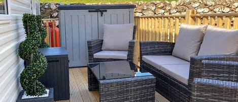 Een overdekt terras met rieten meubels en een stenen achtergrondmuur.