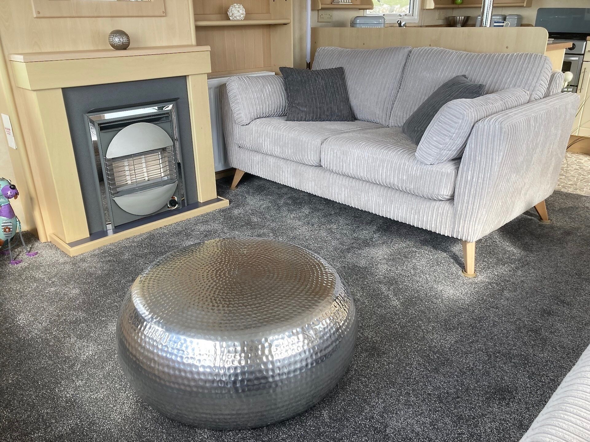 A living room with a grey sofa, a round ottoman, and a fireplace.
