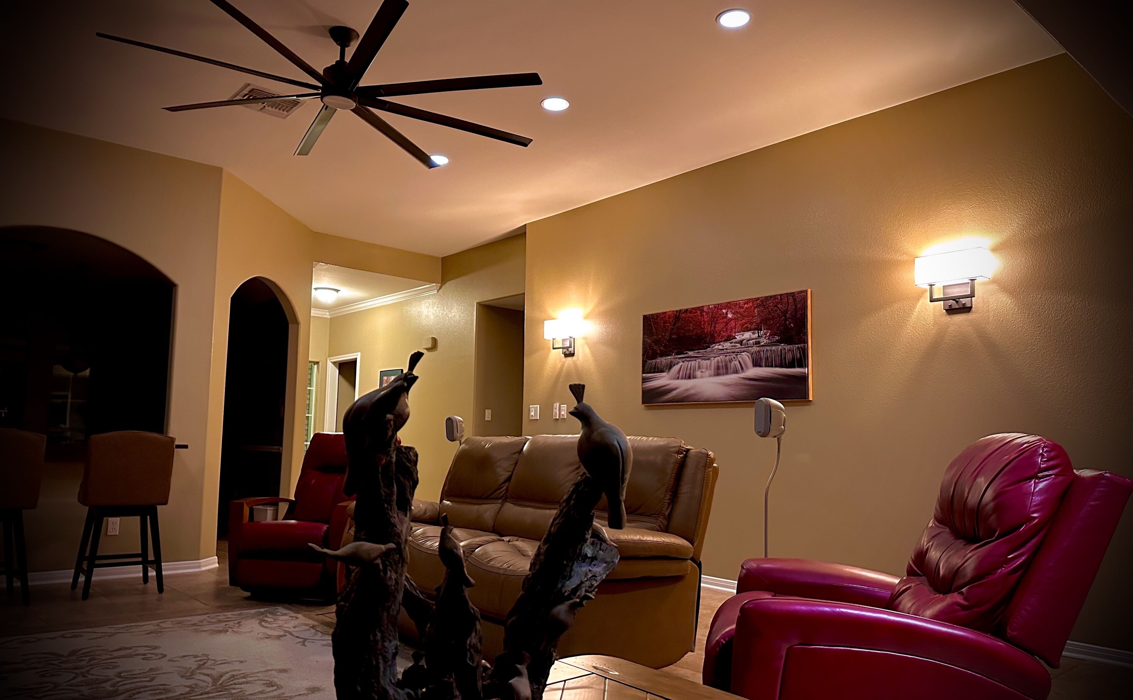 A living room with a ceiling fan, a fireplace, a red leather chair, a brown leather sofa, and a painting on the wall.
