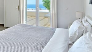 Ein Hotelzimmer mit Bett, weißen Vorhängen, einer Klimaanlage und Blick auf das Meer durch die Glastüren.