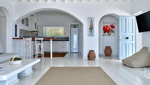 Ein modernes Wohnzimmer mit einer Couch, einem Couchtisch und einem Sitzsack. Im Hintergrund ist eine Küche mit einem Essbereich zu sehen.