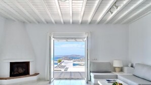 Ein modernes Wohnzimmer mit Kamin, Sofa, Couchtisch und Blick auf eine Küstenlandschaft durch ein großes Fenster.