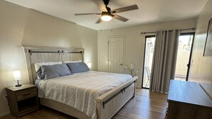 A bedroom with a bed, nightstand, ceiling fan, and a desk.