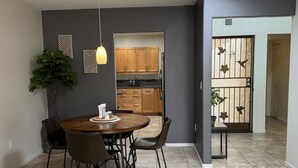 A dining area with a round table and chairs, a potted plant, and a view into the kitchen.