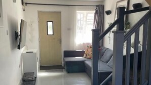 Een woonkamer met een bank, een bijzettafeltje, een deur en een trap.