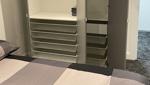 Een slaapkamer met een bed, een kast met kledingrek en een opbergmeubel.