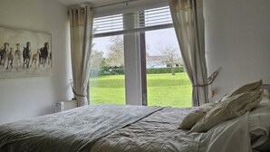 Un dormitorio con una cama grande, un cuadro de caballos en la pared y vista a un césped verde por la ventana.