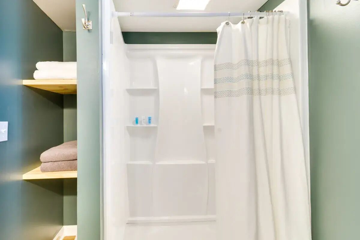 A bathroom with a shower, a towel rack, and a shelf with toiletries.