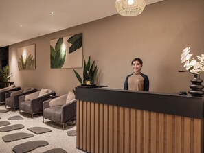 A reception area with a wooden reception desk, a large plant, and a wall-mounted artwork. - CLASSYC Hotel (Hanoi)