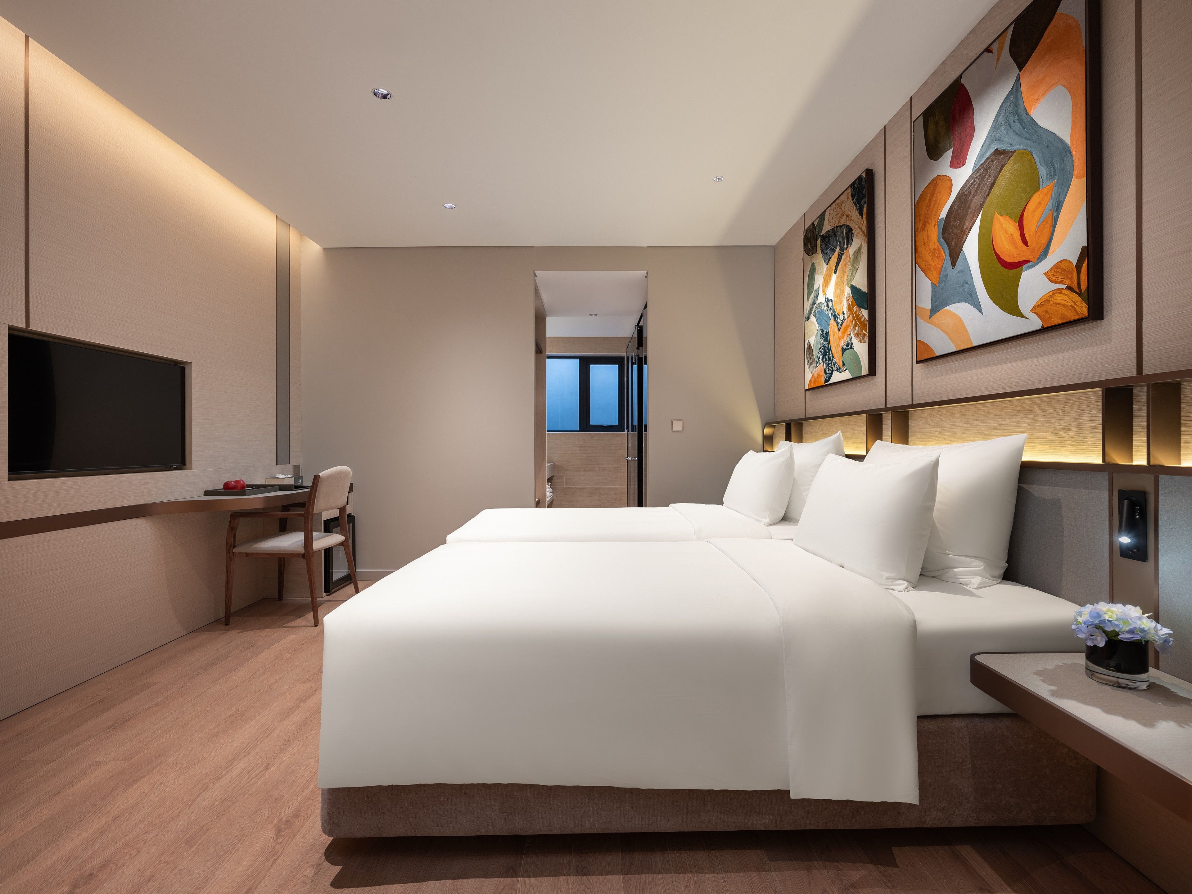 A modern hotel room with a large bed, a desk, a chair, and a flat-screen TV.