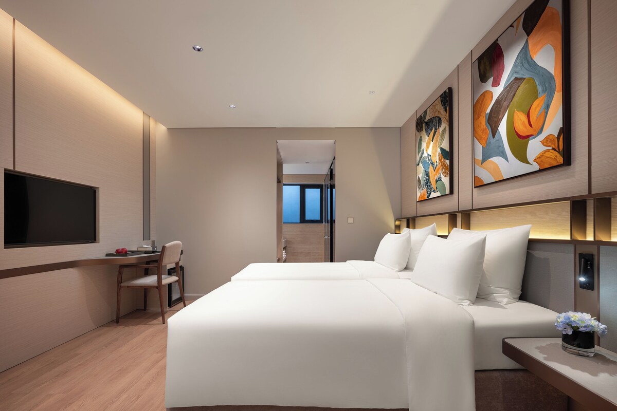 Una habitación de hotel moderna con una cama grande, un televisor de pantalla plana, un escritorio y un cuadro en la pared.