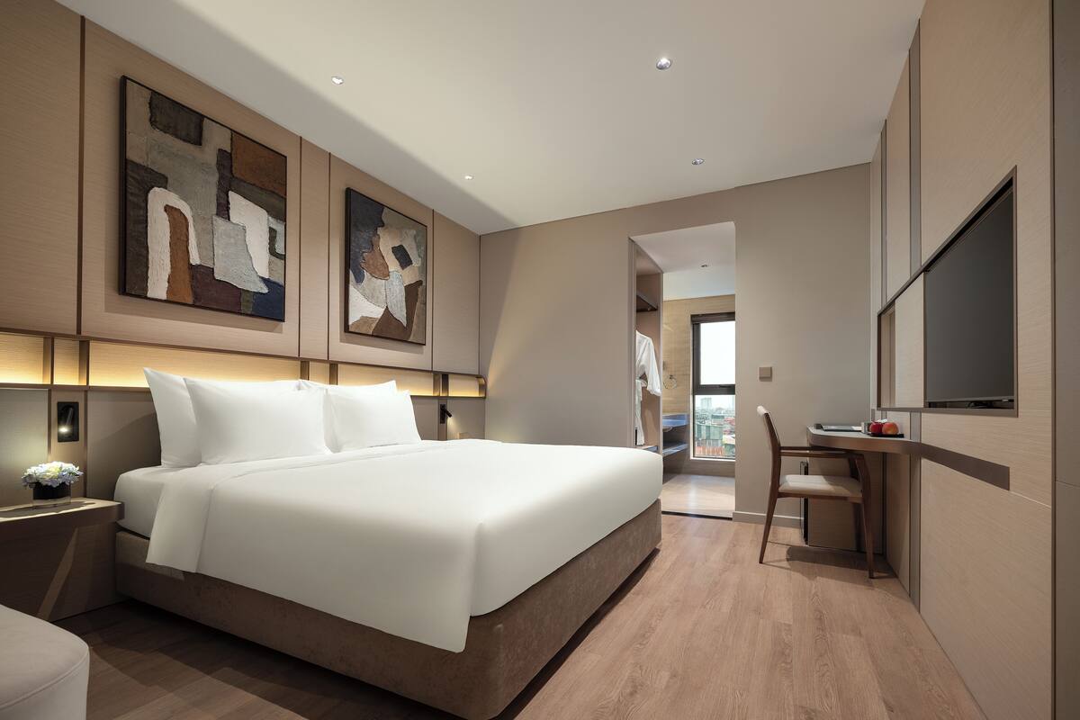 A modern hotel room with a large bed, a desk, and artwork on the walls.